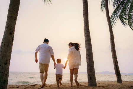 Asian family with fathers, mother and son are walking along a beachfront beach with coconut trees while on vacation in the summer in Thailand.の写真素材