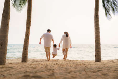 Asian family with fathers, mother and son are walking along a beachfront beach with coconut trees while on vacation in the summer in Thailand.の写真素材