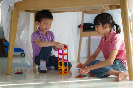 Asian sibling playing building block while sitting in a blanket fort in living room at home for perfect hideout away from their other family members and for them to play imaginatively.の写真素材
