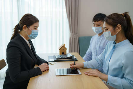 Asian woman's real estate agents are having clients sign contracts to sell their homes in digital tablet while wearing marks to prevent the spreadの写真素材