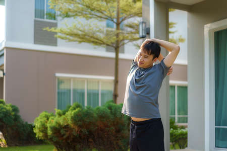 Asian man stretching to warm up or cool down, before or after exercise, near the front door in the neighborhood for daily health and well being, both physical and mental.の写真素材