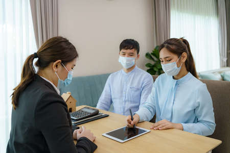 Asian woman's real estate agents are having clients sign contracts to sell their homes in digital tablet while wearing marks to prevent the spreadの写真素材