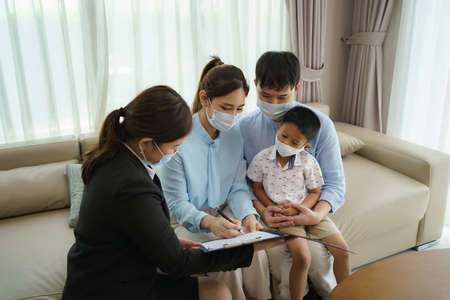 Asian woman's insurance broker is offering details of health insurance coverage for    Asian family with father, mother and son in their living rooms at home.の写真素材