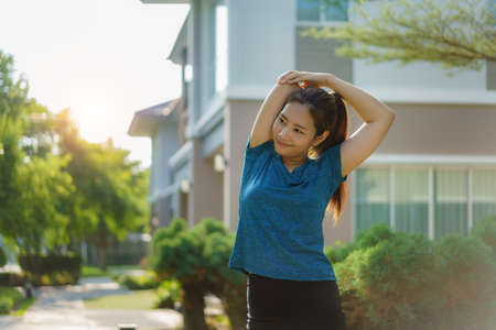 Asian woman stretching to warm up or cool down, before or after exercise, near the front door in the neighborhood for daily health and well being, both physical and mental.の写真素材