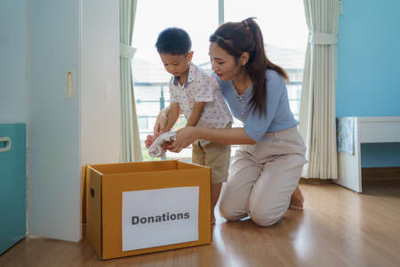 Asian mother and son are standing near closet of clothes in the dressing room carrying a box of clothes donated to take to the donation center.の写真素材