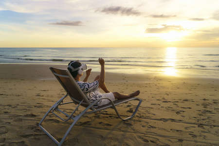 Young Asian man using virtual reality glasses for business meeting on the tropical beach over beautiful sea and sky backgroundの写真素材