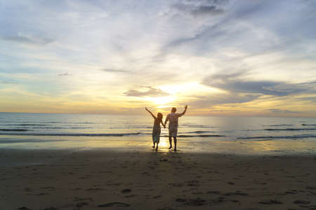 Asian woman traveler holding man's hand and looking beautiful sunset on the beach, Couple on vacation in summer and freedom conceptの写真素材