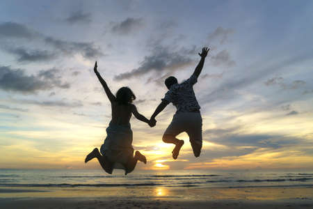 Asian couple jumping on the beach near sea with beautiful sunset, Couple on vacation in summer holidays conceptの写真素材