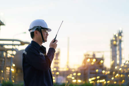 Asian man technician Industrial engineer using walkie-talkie and holding bluprint working in oil refinery for building site survey in civil engineering project.の写真素材