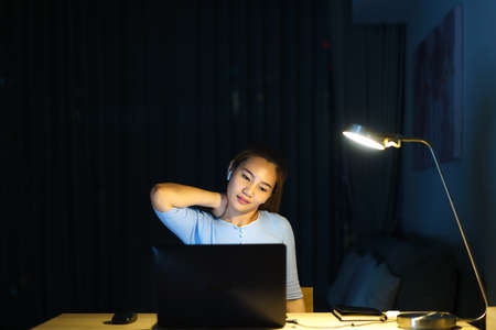 Asian woman are stretch lazily while working long hours in front of a computer in late night in living room at home.の写真素材