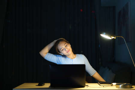 Asian woman are stretch lazily while working long hours in front of a computer in late night in living room at home.の写真素材