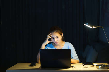 Asian woman work late at night stressful with project research problems on a laptop computer or notebook at home office  burnout syndrome concept.の写真素材