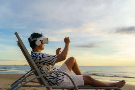 Young Asian man using virtual reality glasses for business meeting on the tropical beach over beautiful sea and sky backgroundの写真素材