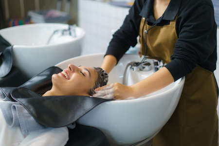 hairdresser is applying shampoo and massaging hair of a customer. Woman having her hair washed in a hairdressing salon.の写真素材