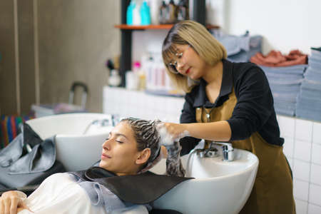 hairdresser is applying shampoo and massaging hair of a customer. Woman having her hair washed in a hairdressing salon.の写真素材