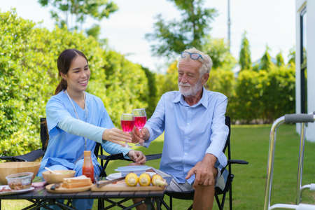 Caucasian handicapped elderly people with mobility walker camping with Asian woman caregivers at home garden to relax and experience nature in the summer.の写真素材