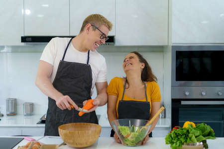 Romantic couple is cooking in the kitchen. A handsome man and a charming woman are having fun together while making healthy lifestyle ideas salad.の写真素材