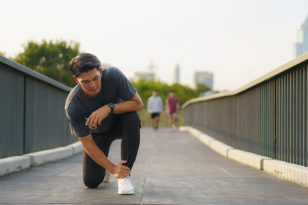 Asian Runner suffering ankle injury after sport outdoors in a city outskirts park