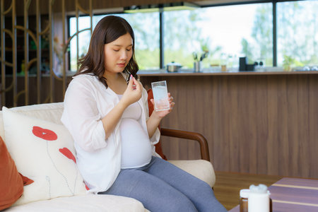 Asian woman pregnant mother holding medicine supplement drugs and glass of water - taking vitamins during pregnancyの写真素材