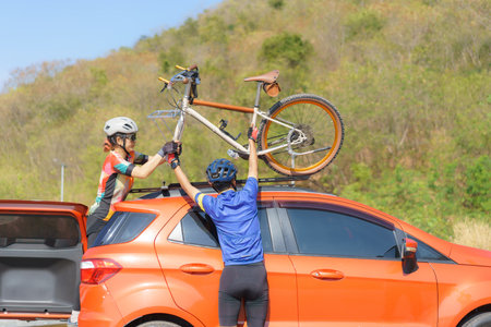 Asian cyclist couple unloading their bicycles from the roof of their car in preparation for a...