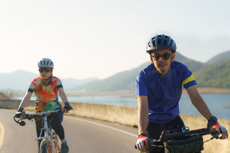 Asian cyclist couple riding together for exercise around the lake in the morning with beautiful mountain view in the background.の写真素材