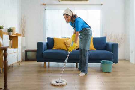 Diligent Asian housewife meticulously mops the living room, epitomizing dedication and determination in maintaining a clean and tidy home.の写真素材
