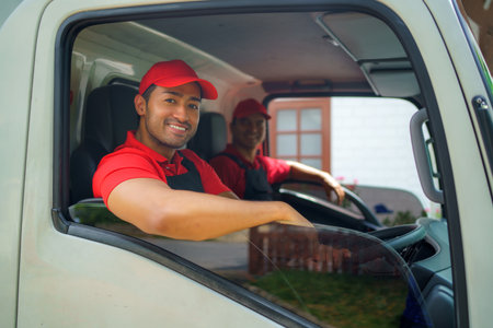 Transport worker sits in the cargo truck, smiling with readiness and dedication as they embark on the move to a new house. Their enthusiasm and commitment to service ensure a seamless and joyful transition for the homeowners.の写真素材