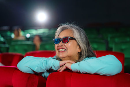 Asian elderly women with glasses eagerly watch 3D movies, popcorn in hand, relishing the immersive...