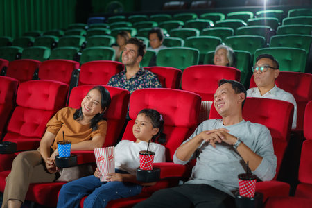 Happy Asian family of father, mother, daughter, and grandmother cherishes weekend moments at the cinema, sharing joy and togetherness while watching a movie.の写真素材