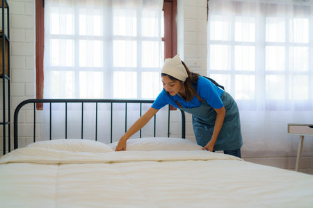 In the tranquil bedroom, an Asian housewife meticulously arranges blankets, infusing warmth and order, turning a bed into a cozy oasis of comfort.の写真素材