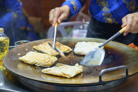Immerse yourself in the bustling streets of Thailand with this vibrant scene. A skilled vendor expertly prepares crispy roti, a beloved street food delicacy, delighting passersby with its enticing aroma and mouthwatering taste. Experience the essence of Thai culinary tradition in every biteの写真素材