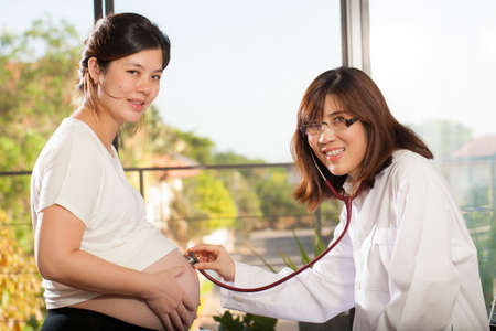 Pregnancy, an Asian doctor use stethoscope check at pregnancy belly of Asian woman