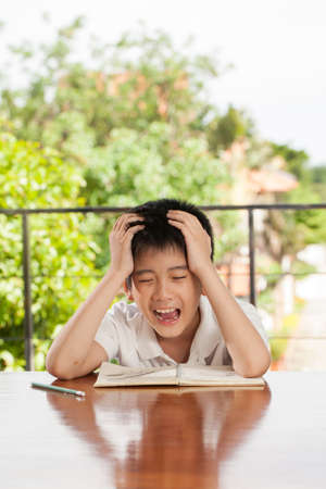 headache boy an Asian young boy squeeze his head for homework like crazyの写真素材