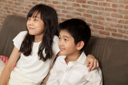 family Asian Thai relatives brother and sister sit on a sofa together playing gameの写真素材
