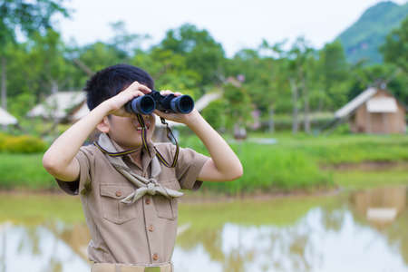 Boy Scout, a Thai Asian young boy scout in uniform exploring with binocular in the forestの写真素材