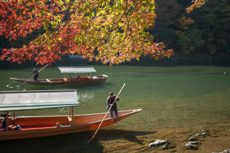 Kyoto,Japan, November 6,2015 A sightseeing boat with passengers rowing in Katsura River with red maple tree, Kyoto, Japanのeditorial素材