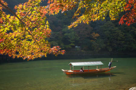 Kyoto,Japan, November 6,2015 A sightseeing boat with passengers rowing in Katsura River with red maple tree, Kyoto, Japanのeditorial素材