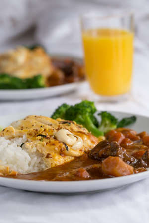 Japanese curry, a colourful dish of Japanese curry rice with omelette and broccoli with a glass of orange juice.の写真素材