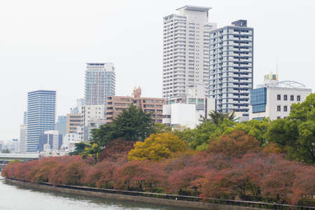 OSAKA, JAPAN - NOVEMBER 13,2015  Public park by the Okawa river at Osaka Castle in red Autumn with building in business zone Osaka, Japanのeditorial素材