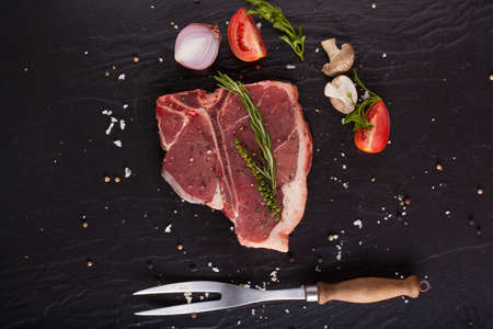 T-Bone fillet, red fresh raw fillet of T-Bone steak cut seasoning salt pepper and rosemary with fork on black background.の写真素材
