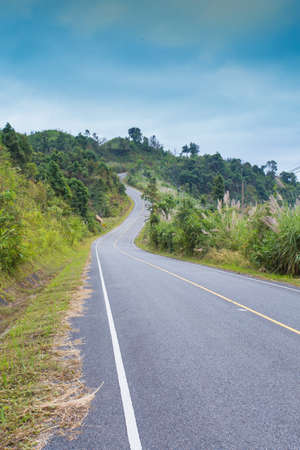 country road side, curve road along corn field and fence with mountain scenery in country side,...