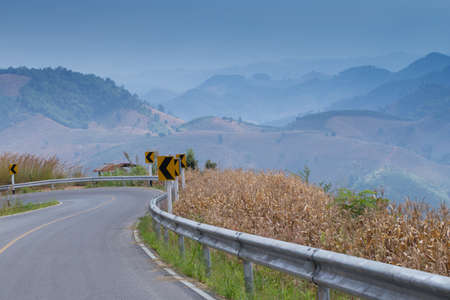 Curve road along corn field and fence with mountain scenery in country side, Thailandの写真素材