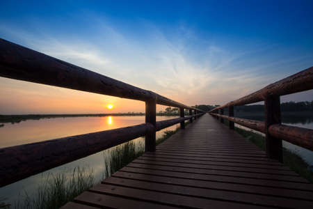 Long road on the wooden bridge by the lake with silhouette of dramatic colour sunrise sky, Thailandの写真素材