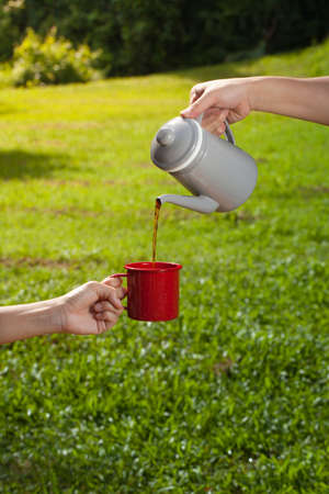 hands pouring coffee from a jar to a glass at green grass floor.の写真素材