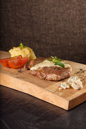 A prepared piece of steak cut with blue cheese sauce on dining table utensils decorated.の写真素材