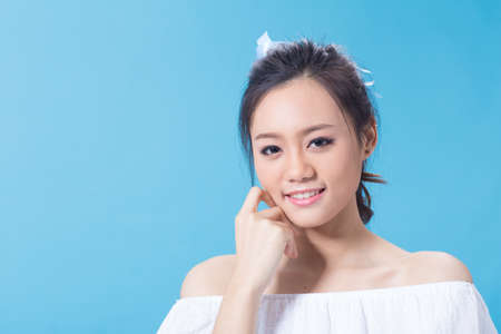 Asian cute young girl holding cosmetic product in white shirt showing her skin in light blue backgroundの写真素材