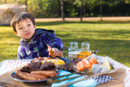 An Asian cute young boy eating breakfast outdoor at camping site in nature sunlight with a tent at the background.の写真素材