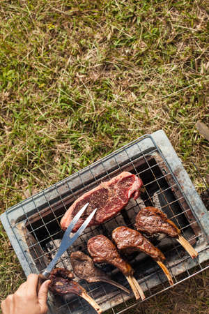 Herb seasoning Lamb rack and beef grilled on charcoal stove outdoor on the grass ground with kitchen equipment knife and fork.の写真素材