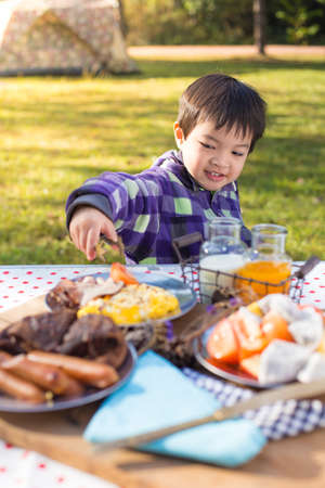 An Asian cute young boy eating breakfast outdoor at camping site in nature sunlight with a tent at the background.の写真素材