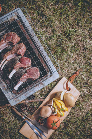 Herb seasoning Lamb rack and beef grilled on charcoal stove outdoor on the grass ground with kitchen equipment knife and fork.の写真素材
